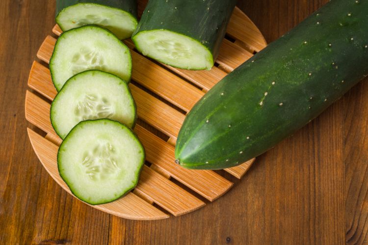 Foto de pepino cru inteiro e fatiado sobre mesa de madeira
