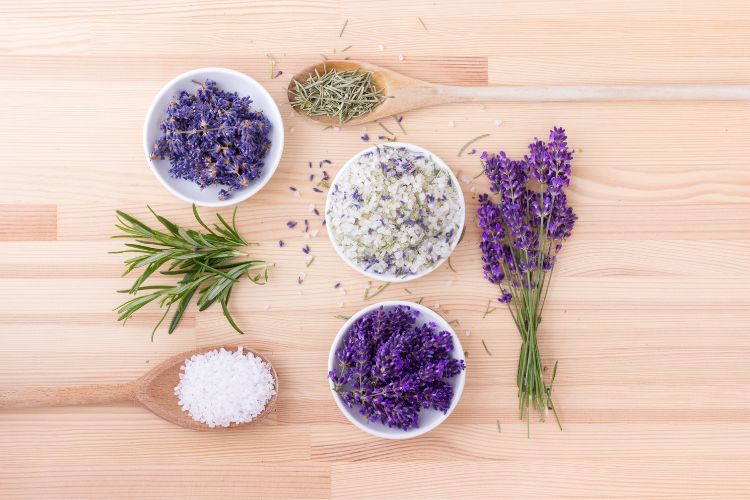 Foto de mesa de madeira com lavanda, sal grosso, colheres, potes com sal e lavanda, além de alecrim