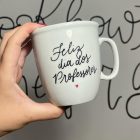 Pessoa de pele clara segurando caneca escrito "Feliz Dia Dos Professores"