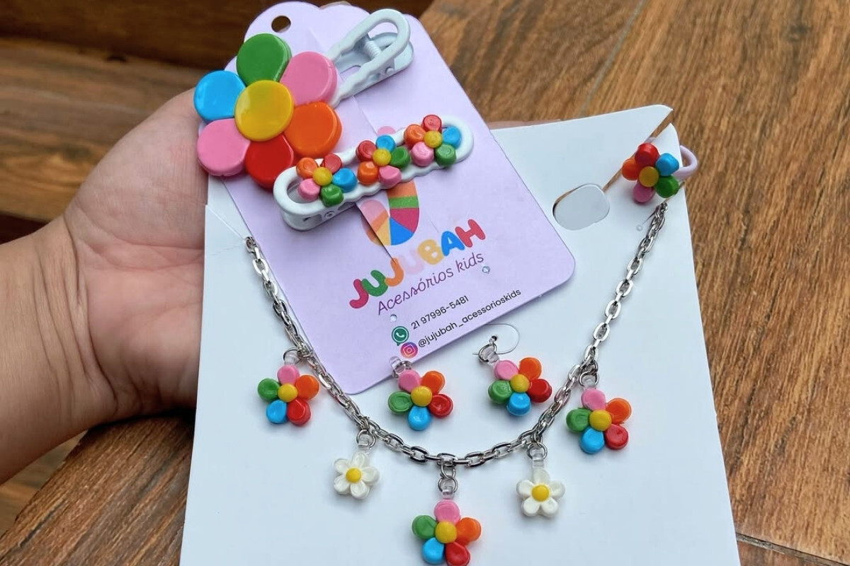 Um conjunto de bijuterias infantis coloridas com tema de flores. O kit inclui um colar com pingentes de flores e brincos combinando, além de presilhas para cabelo e um anel, todos com flores multicoloridas.