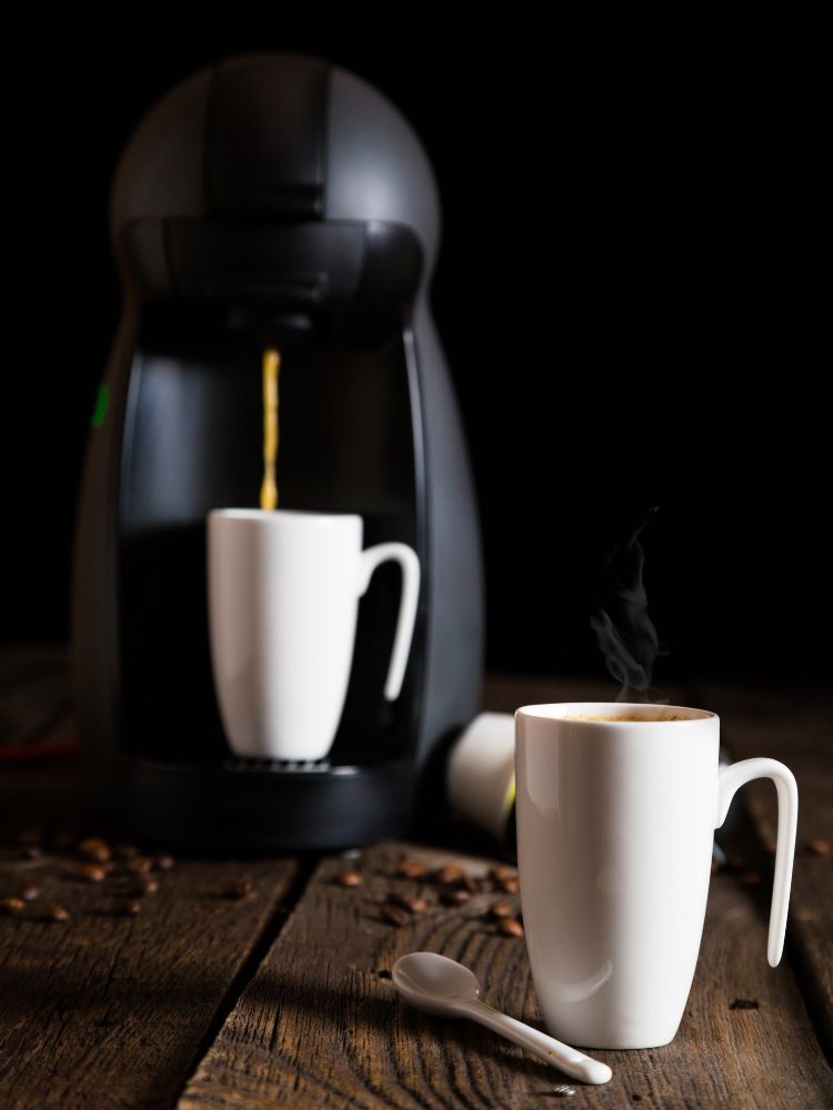 Foto de máquina preta da Dolce Gusto com duas xícaras de café brancas