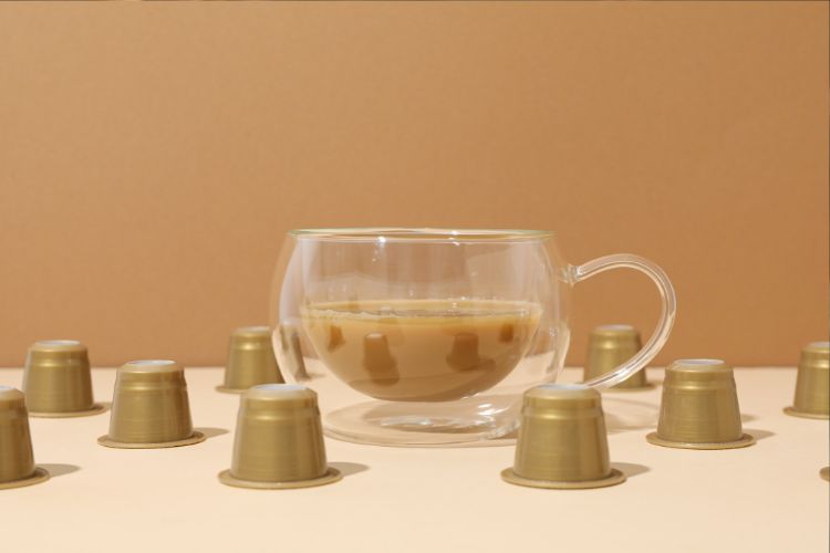 Xícara de vidro com chai latte e cápsulas douradas em volta