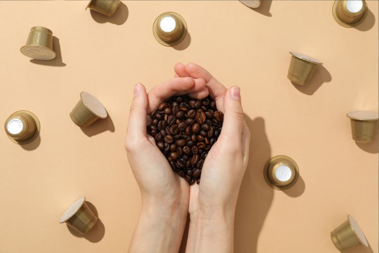 Mãos de mulher segurando grãos de café com cápsulas douradas da Dolce Gusto em volta
