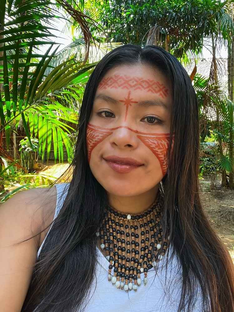 Maira Gomez usando pintura vermelha no rosto, colares e blusa branca