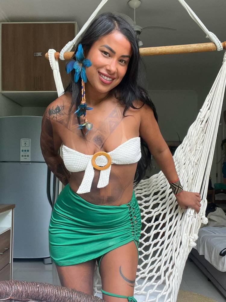 Kae Guadajajara usando brinco azul de flor, top branco e saia verde drapeada
