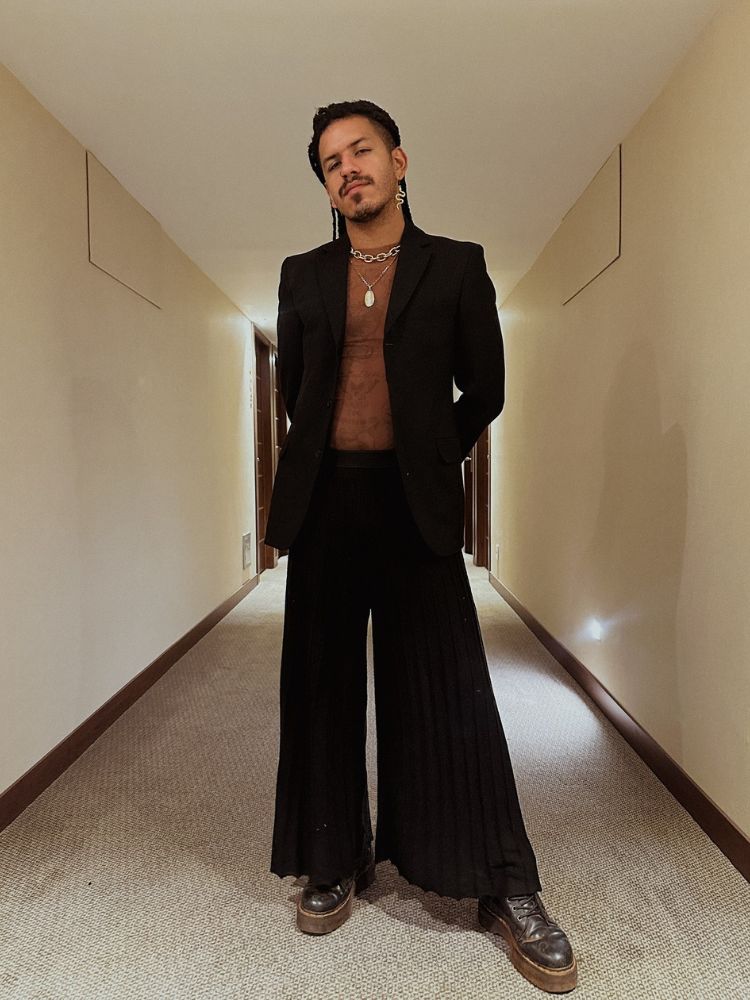 Spartakus Santiago usando blusa marrom, blazer preto e calça preta