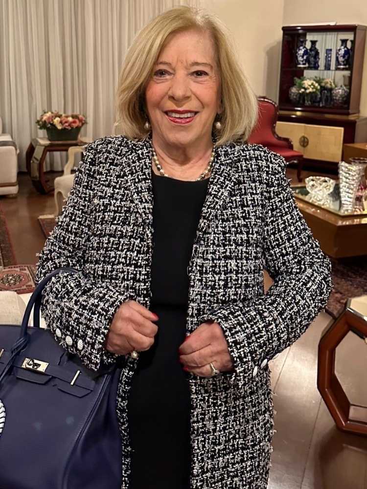 Maria Berklian usando look preto e casaco preto e branco, além de bolsa azul marinho