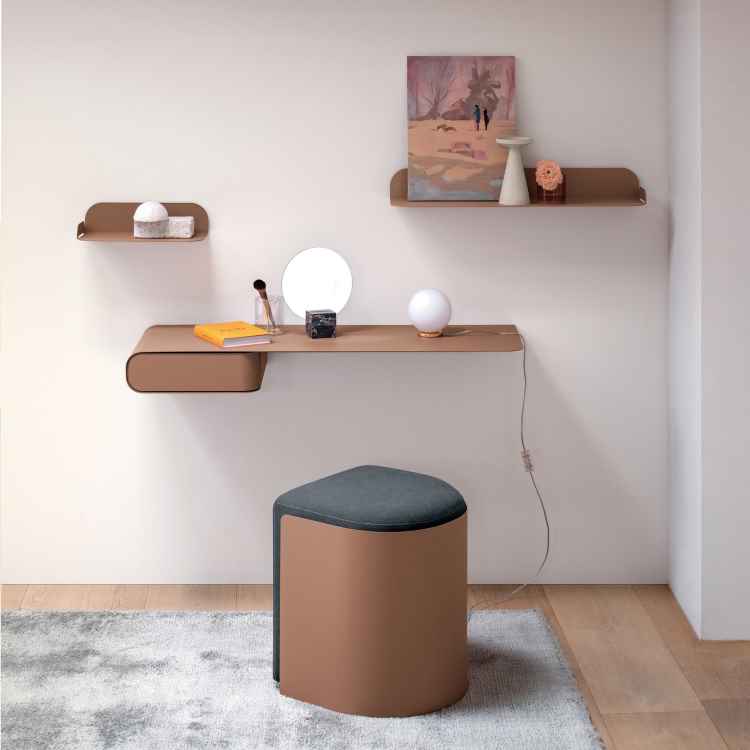 Espaço minimalista com prateleiras flutuantes em madeira clara cor Mocha Mousse. Mesa suspensa abriga objetos decorativos, incluindo espelho redondo e luminária esférica. Um banco estofado em tecido escuro contrasta suavemente com o chão de madeira clara e tapete neutro, criando um ambiente funcional e elegante.