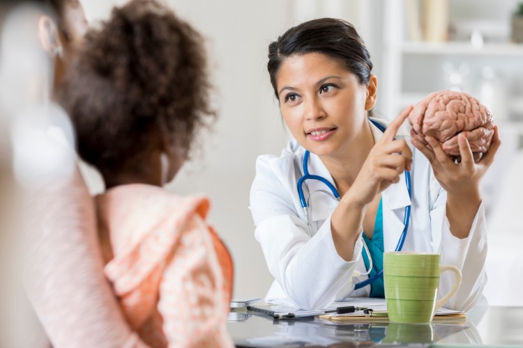 Médica de pele morena com imitação de cérebro na mão, mostrando para a mãe e filha
