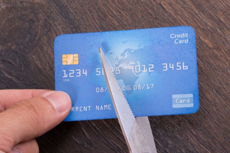 Pessoa de pele clara cortando cartão azul de crédito ao meio com uma tesoura