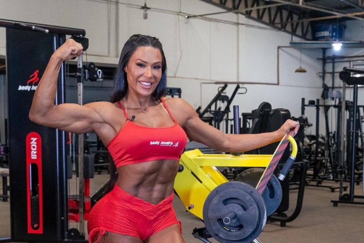 Gracyanne Barbosa na academia usando top e shorts vermelho, fazendo pose mostrando o bíceps