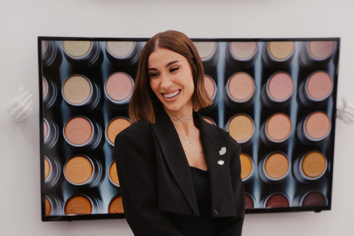 Boca Rosa de terno preto sorrindo, com foto de seus tons de base ao fundo