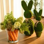 Foto de arranjo de flores e cenouras ao lado de coelhos feitos de musgo