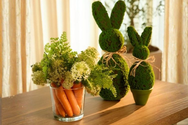 Foto de arranjo de flores e cenouras ao lado de coelhos feitos de musgo