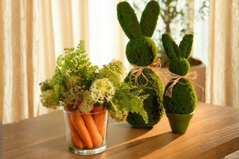 Foto de arranjo de flores e cenouras ao lado de coelhos feitos de musgo