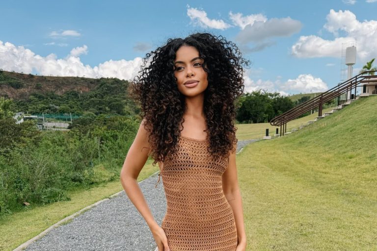 Steffany Borges usando vestido de crochê marrom no campo, exibindo seus cabelos castanhos cacheados