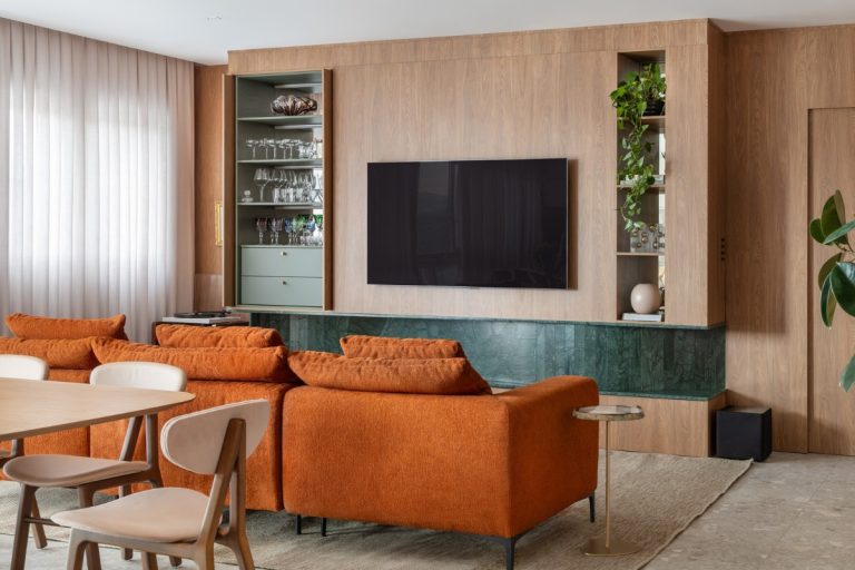 Sala de TV com painel de madeira, nichos com vasos, cristaleira embutida, sofá terracota, mesa bege