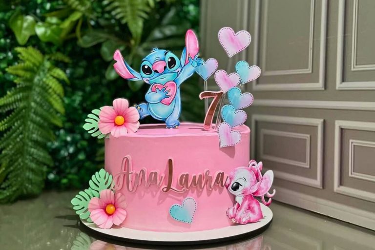 Um bolo de aniversário rosa vibrante decorado com o personagem Stitch azul segurando um coração, um Stitch rosa bebê e vários corações em tons de rosa e azul-claro. O bolo tem a idade "7" e o nome "Ana Laura" em destaque. Fontes