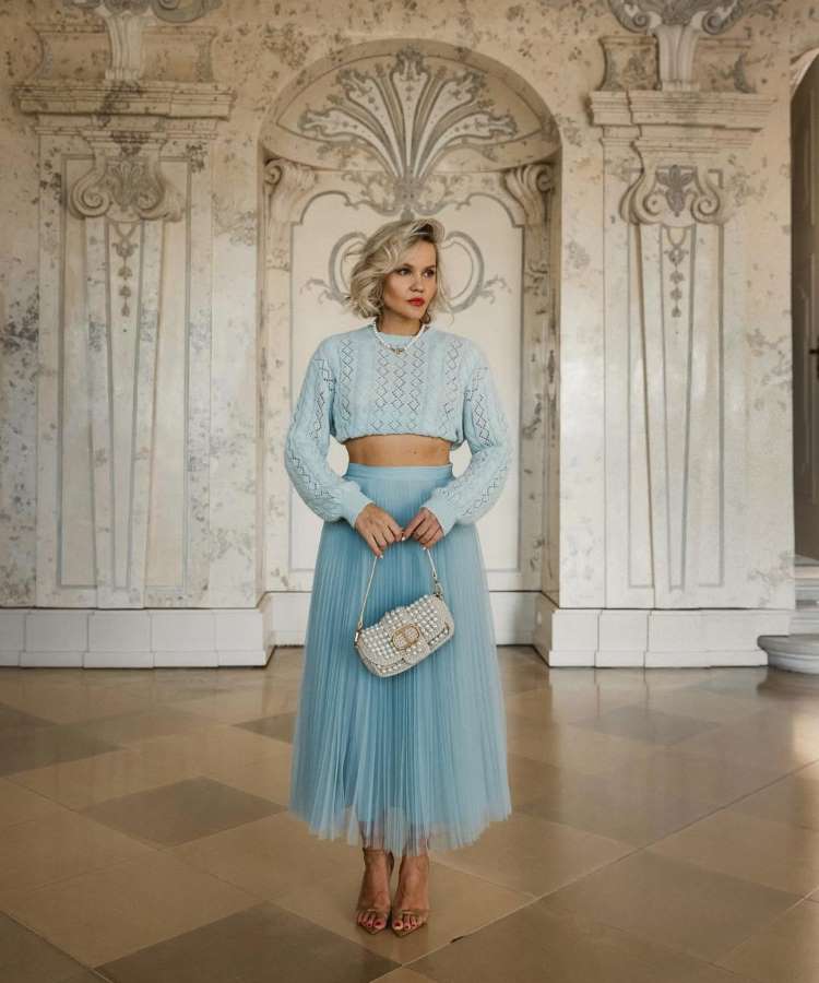 Conjunto de duas peças em azul claro, com um top de tricô cropped e uma saia midi de tule plissada. A combinação de texturas e o tom pastel criam um visual delicado e elegante, ideal para casamentos diurnos no inverno.