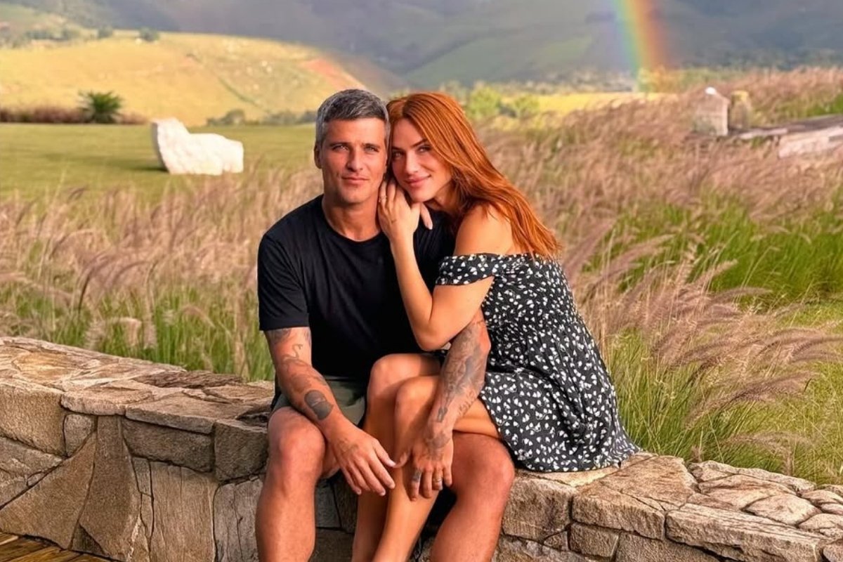 Bruno Gagliasso e Giovanna Ewbank posam em um cenário campestre. Giovanna está sentada no colo de Bruno, que a abraça. Um arco-íris pode ser visto ao fundo. A paisagem é composta por vegetação.
