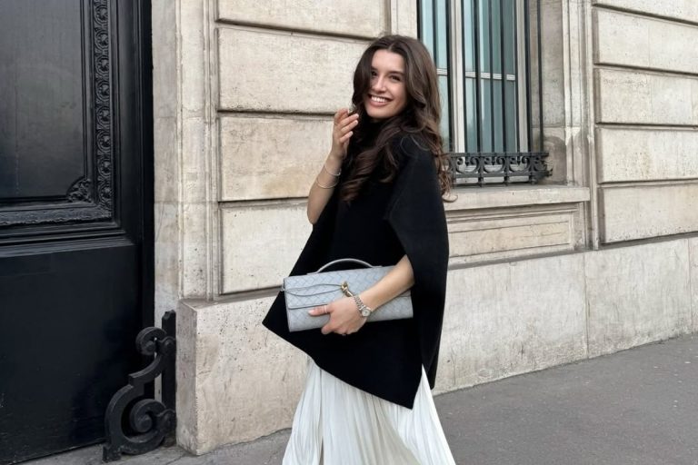 Foto de mulher morena usando poncho preto, saia longa branca e bolsa de mão cinza
