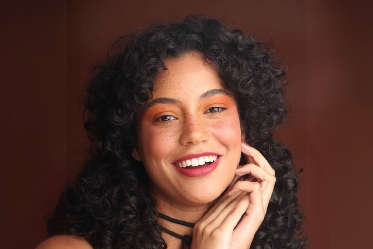 Mulher de cabelo cacheado usando make em tons alaranjados com sarda fake