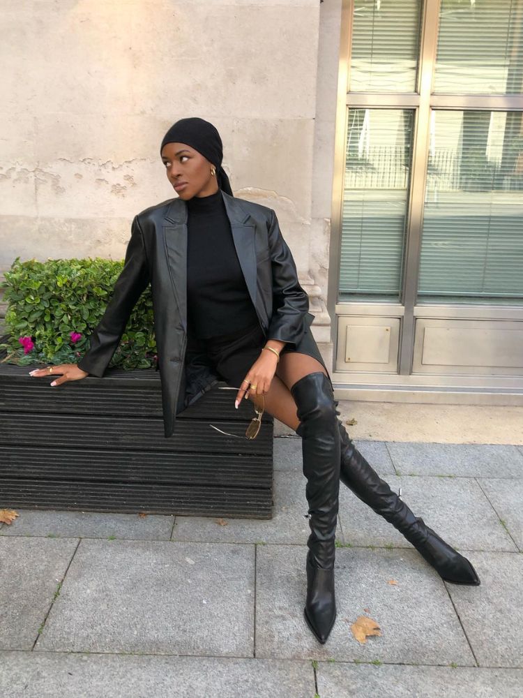 Mulher de pele negra com vestido mini preto, blazer e bota over the knee preta