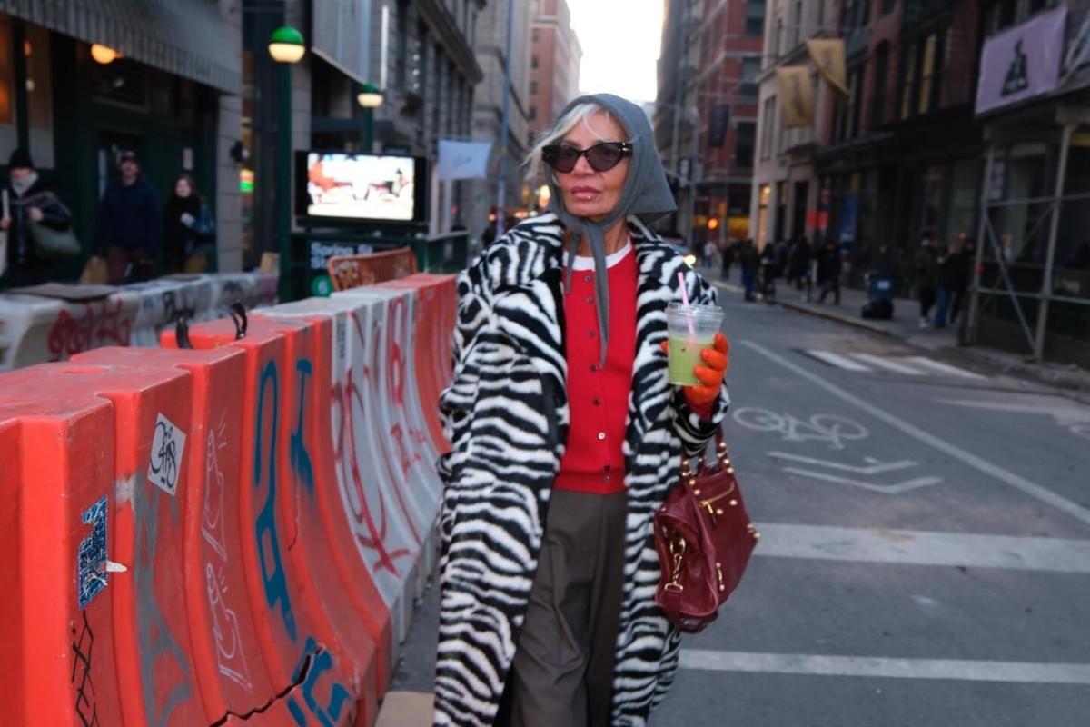 Senhora de pele clara com blusa vermelha, calça de alfaiataria cinza, casaco de zebra, lenço na cabeça
