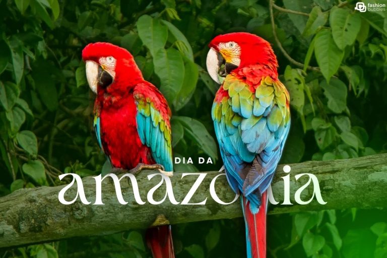 Duas araras-vermelhas vibrantes, com penas vermelhas, azuis e verdes, empoleiradas em um galho de árvore. Ao fundo, folhagens verdes da floresta amazônica. No centro, o texto "DIA DA AMAZÔNIA" celebra a data. A imagem destaca a rica biodiversidade da Amazônia.