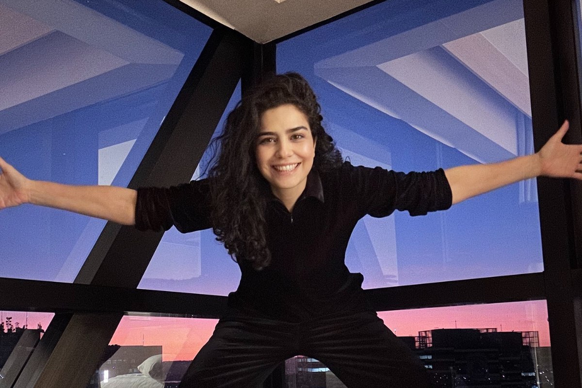 Leticia Sabatella de look preto, sorrindo, de braços abertos, com grandes janelas ao fundo