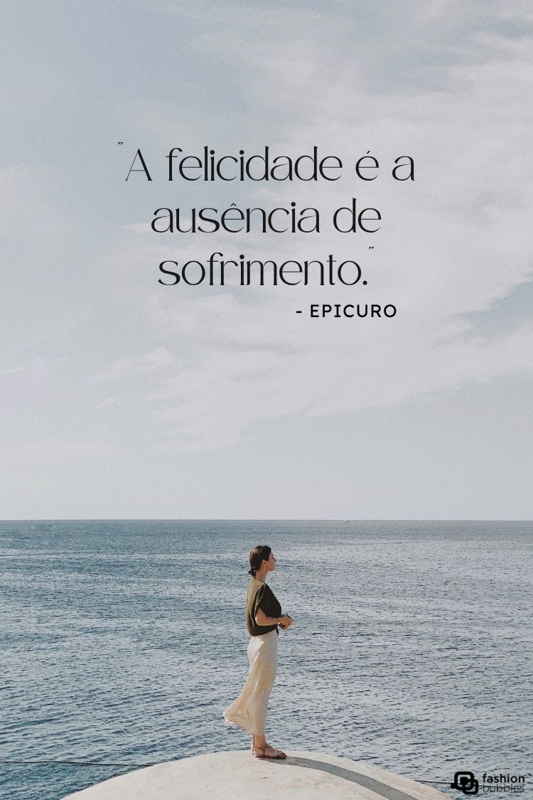 A imagem mostra uma citação de Epicuro: "A felicidade é a ausência de sofrimento." O texto está posicionado sobre uma mulher em pé, de costas, olhando para o horizonte do oceano. Ela usa roupas claras e a cena transmite uma sensação de calma e contemplação.