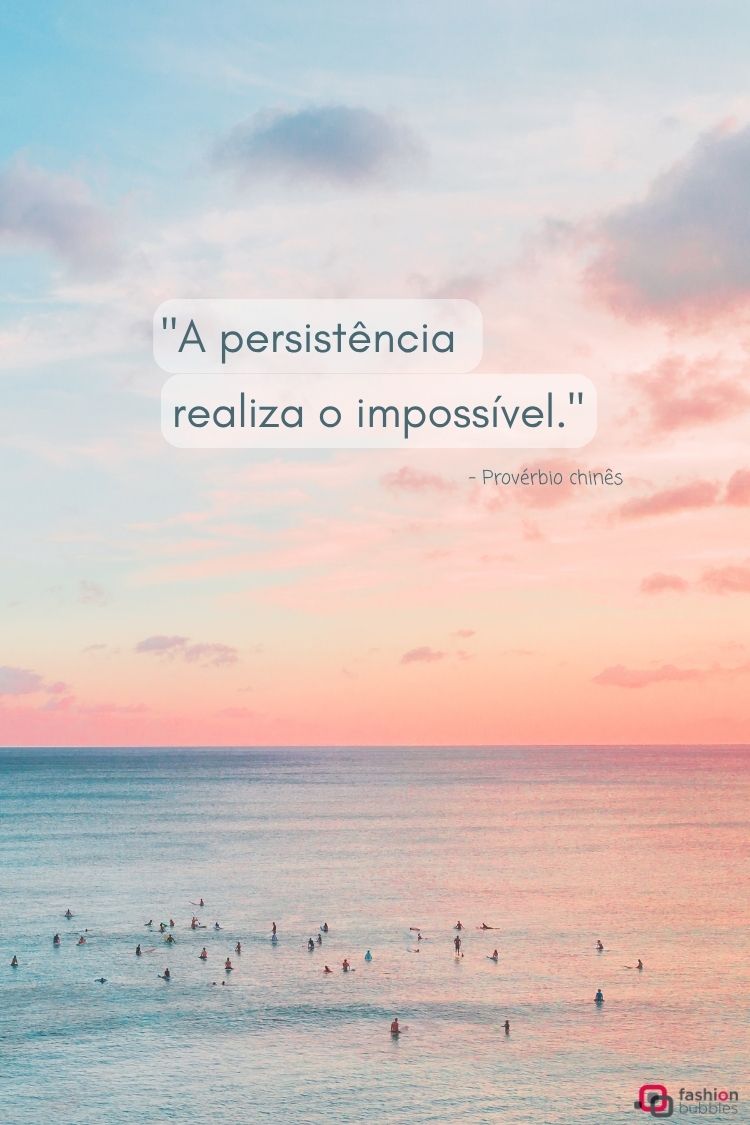 A imagem exibe um provérbio chinês: "A persistência realiza o impossível". O texto está sobreposto a uma paisagem marinha ao pôr do sol, com tons suaves de rosa, laranja e azul no céu e no mar. Pequenas figuras de surfistas e pessoas na água pontuam o oceano calmo, adicionando um senso de tranquilidade.