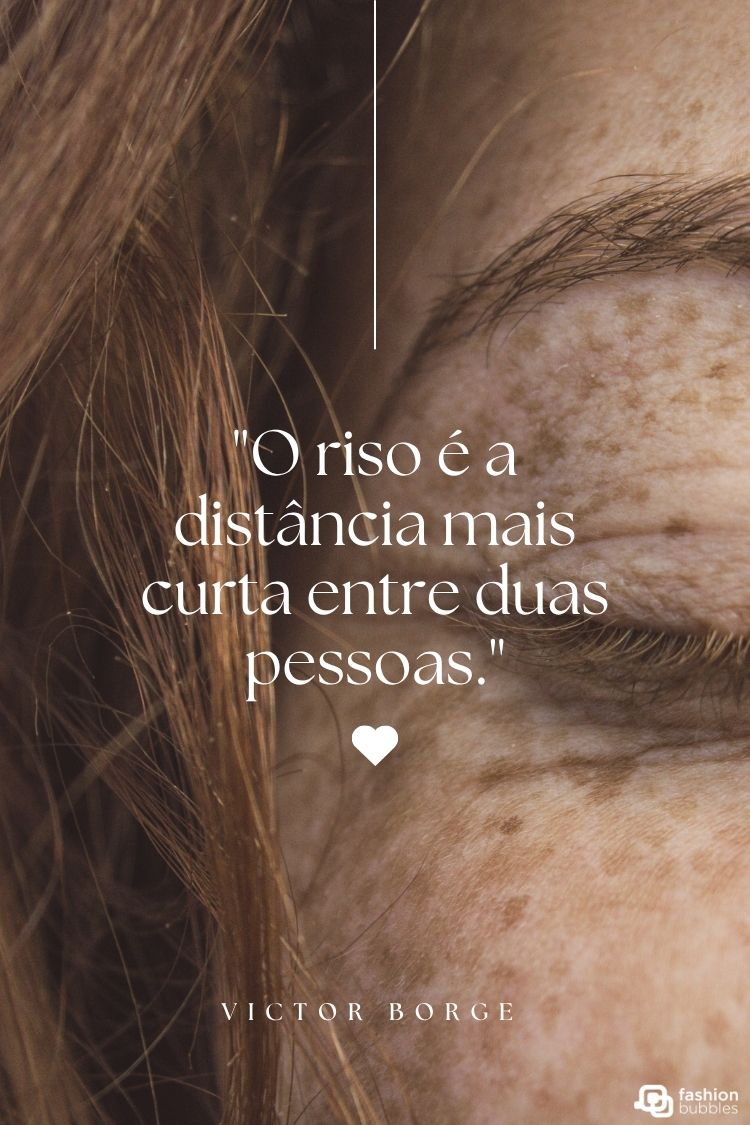 A imagem apresenta a citação de Victor Borge: "O riso é a distância mais curta entre duas pessoas." O texto está sobreposto a um close-up parcial de um rosto com cabelo castanho avermelhado e sardas, focado na área dos olhos e da testa. Um pequeno coração branco complementa a mensagem positiva.