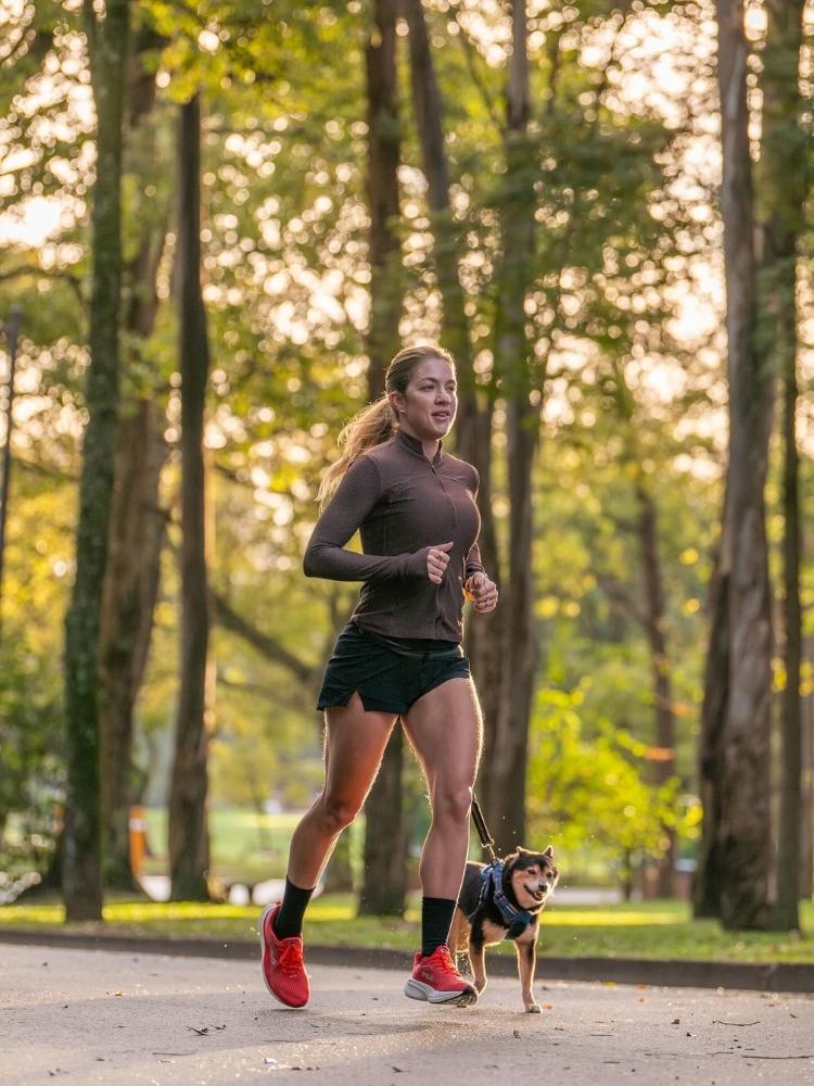 Alana Sicoli correndo em parque com o cachorro, usando jaqueta cinza e shorts preto 