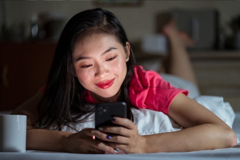 Foto de mulher asiática de cabelos longos usando camiseta vermelha e usando o celular para acessar o Kismia