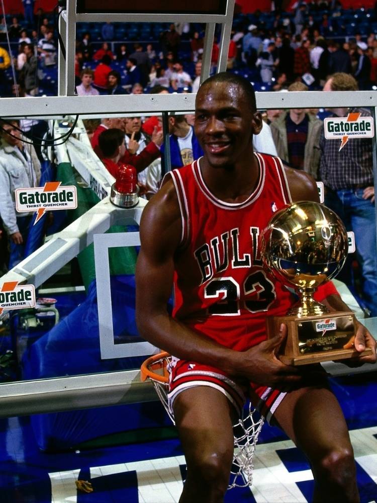 Michael Jordan com uniforme do Chicago Bulls sentado no banco de reservas segurando prêmio