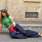Mulher de pele clara deitada na rua usando blusa verde, calça jeans, mocassim cow print de camurça e boné