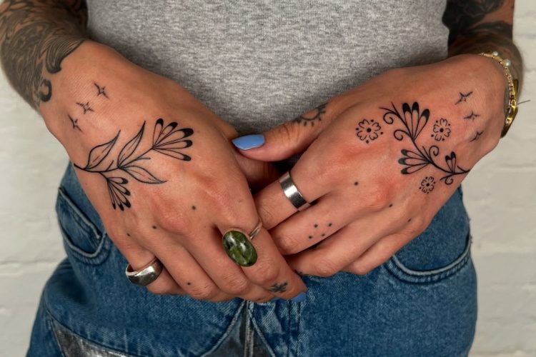 Foto de mãos de mulher de pele clara tatuadas com flores, estrelas e pontos