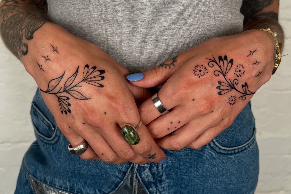 Foto de mãos de mulher de pele clara tatuadas com flores, estrelas e pontos
