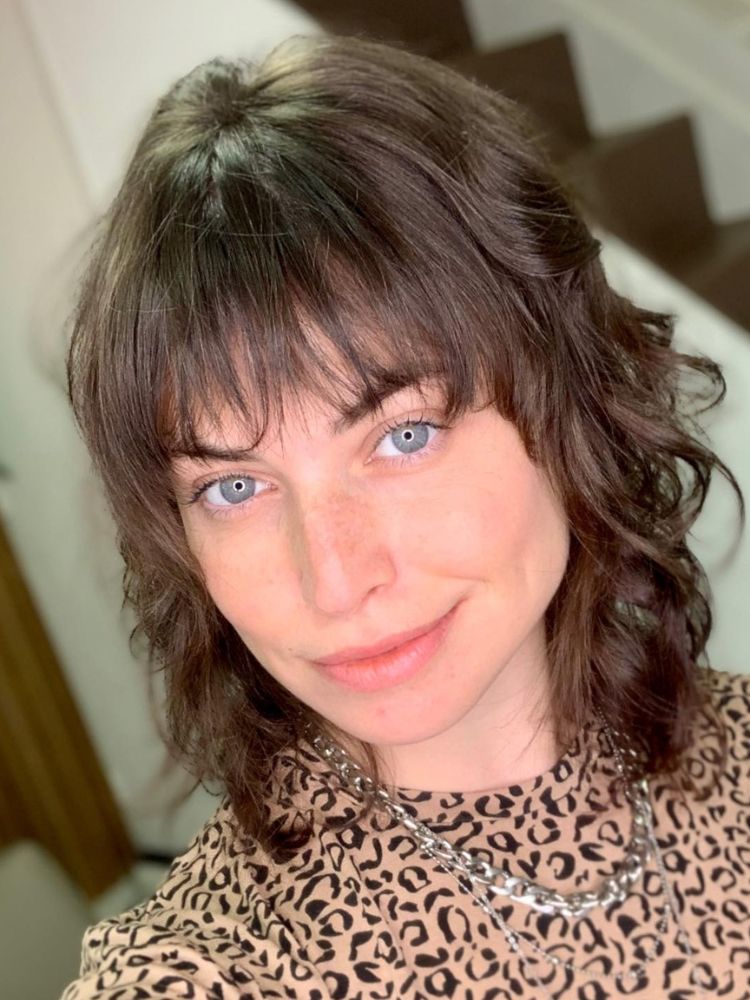 Mulher de olho azul com cabelo castanho curto e franja assimétrica 