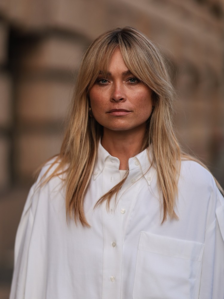 Mulher loira de pele clara com curtain bangs em cabelo abaixo dos ombros 