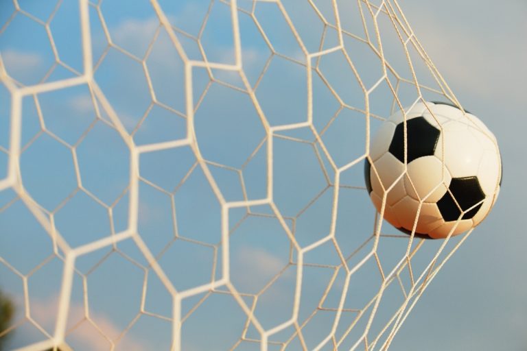 Foto de bola dentro do gol durante partida de futebol ao vivo