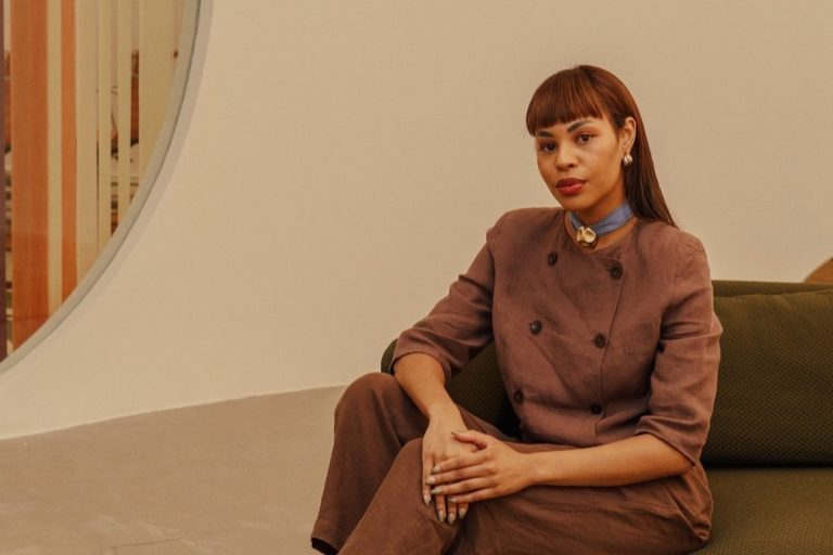 Lari Cunegundes de roupa formal marrom, sentada em sofá marrom