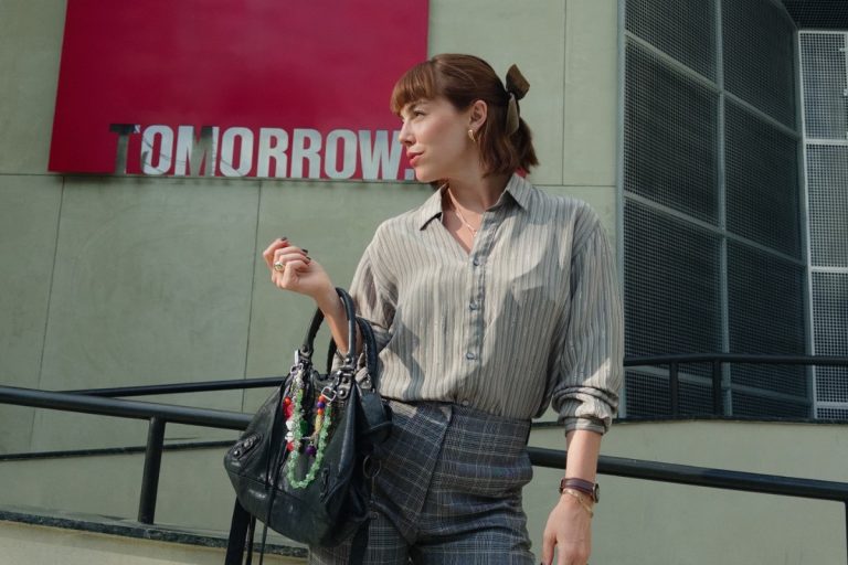 Alice Wegmann usando camisa cinza listrada, calça cinza de alfaiataria, laço no cabelo, em frente à Tomorrow