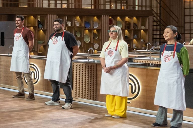 Quatro competidores do MasterChef em uma cozinha. Eles estão em pé, lado a lado, usando aventais brancos de chef com o logotipo do programa. O homem da esquerda e a mulher da direita sorriem.