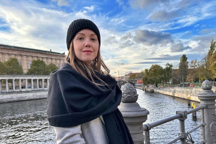 Raquel Real com roupas de frio, apoiada em grande com rio ao fundo