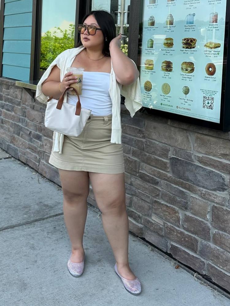 Mulher de pele clara usando tube top branco, saia bege, suéter amarelo-manteiga e sapatilha transparente