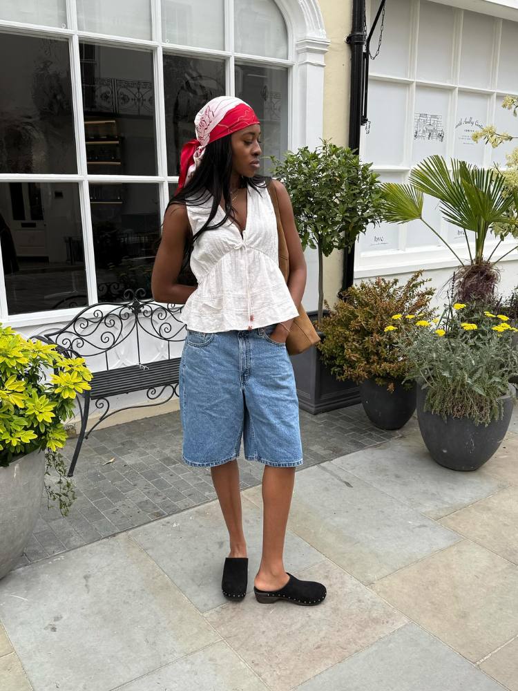 Mulher de pele negra usando blusa branca de amarração, bermuda jeans e clog preta 