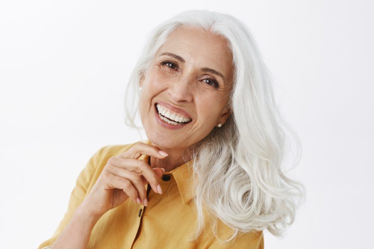 Mulher de pele clara com cabelo branco e camisa mostarda