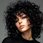 Foto de mulher de cabelo enrolado médio usando blusa preta em fundo cinza